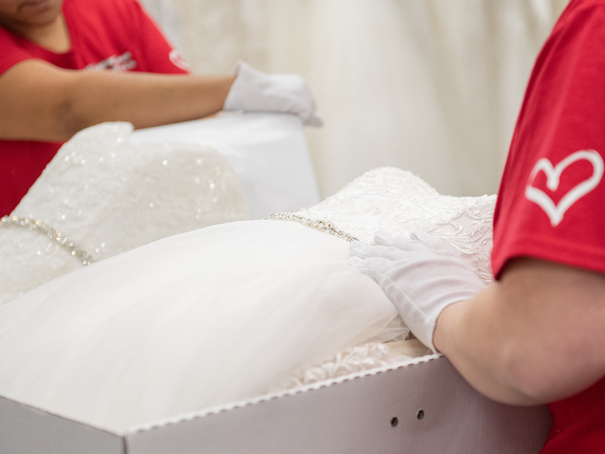Close-up of a wedding dress featuring delicate lace and bead details, with a professional carefully handling the gown to ensure proper preservation.